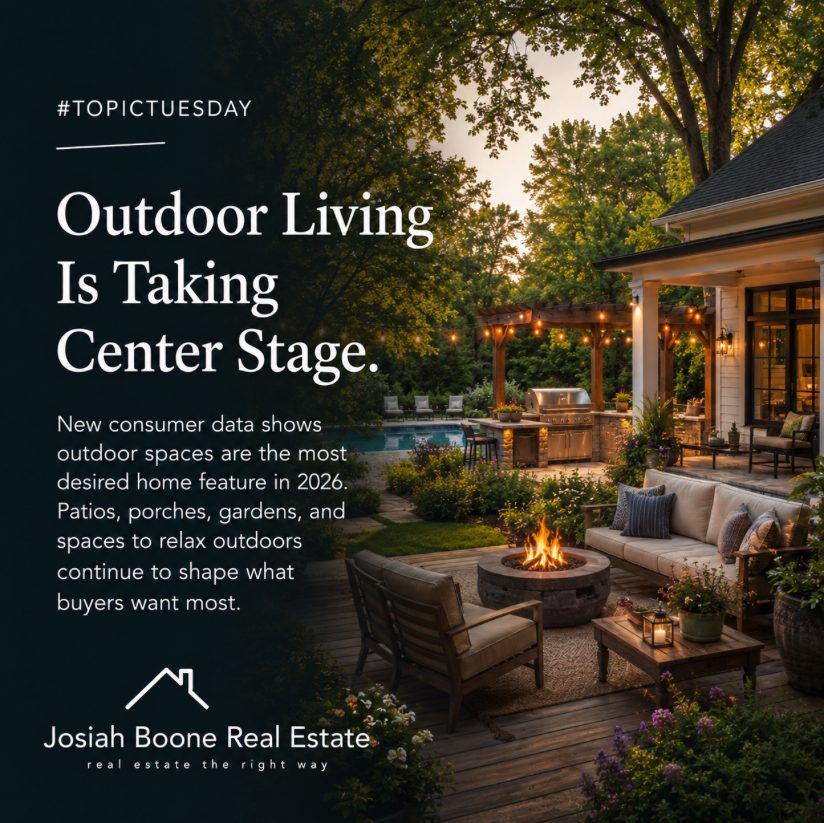 Warm backyard outdoor living space with a low deck, fire pit, patio seating, trees, and inviting evening lighting.