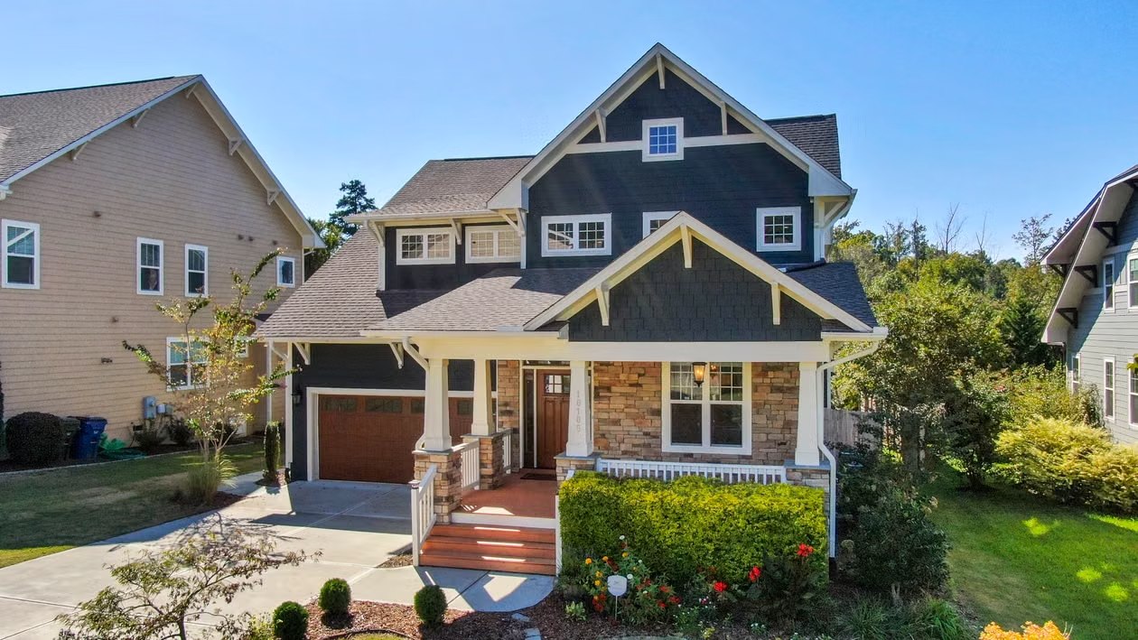 Blue Craftsman-style home with stone accents, a covered porch, and landscaped front yard